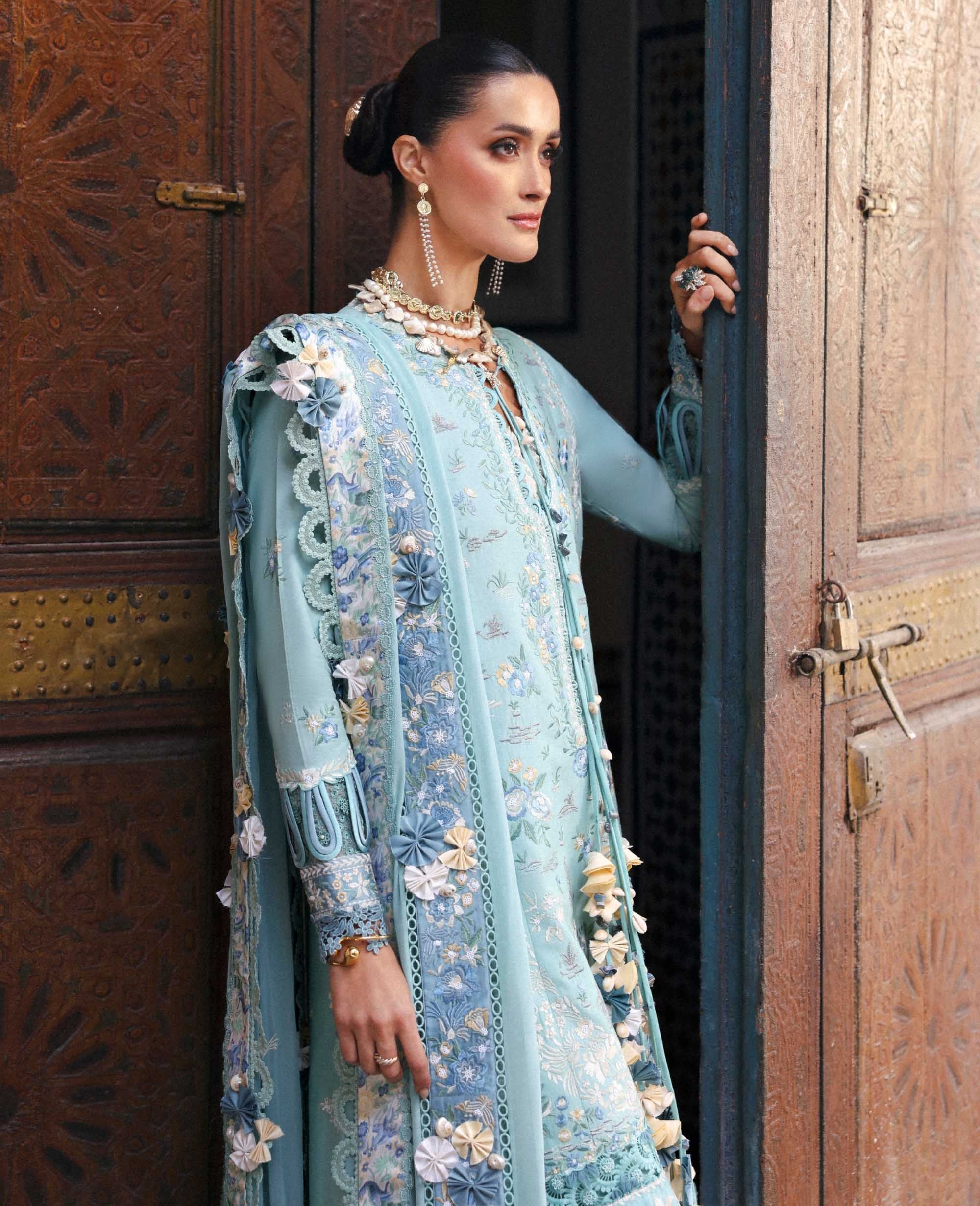 Woman in a light blue embroidered traditional outfit standing in front of a wooden door.