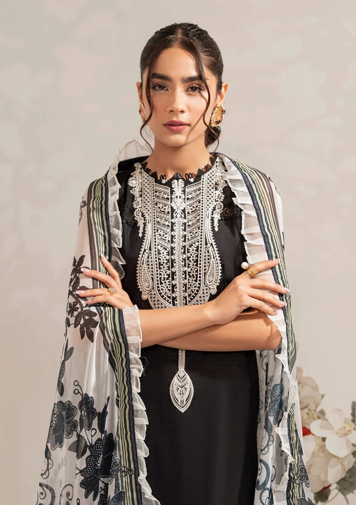 A woman modeling a black traditional outfit with elaborate silver embroidery on the chest and a matching sheer printed dupatta draped over her shoulders.