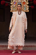 Woman in a traditional outfit with intricate embroidery and jewelry, standing on a red carpet.