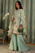 A woman models a traditional light mint green three-piece salwar kameez suit with floral embroidery, wide-leg pants, and a matching sheer dupatta in an ornate room with patterned curtains.
