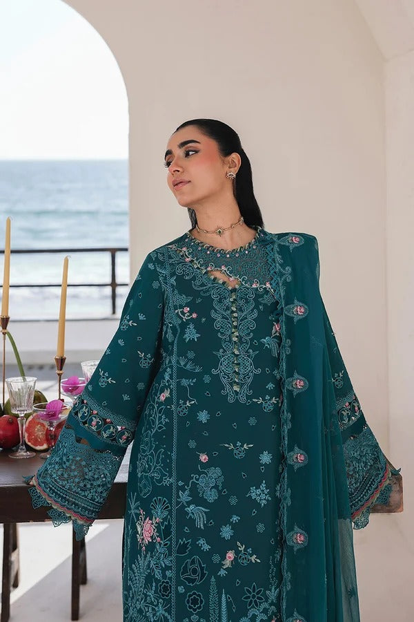Woman wearing a teal embroidered outfit in an indoor setting with ocean view.