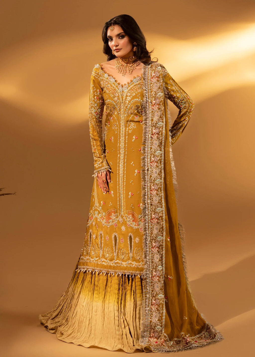 Woman wearing a mustard yellow embroidered traditional outfit with a matching dupatta on a beige background