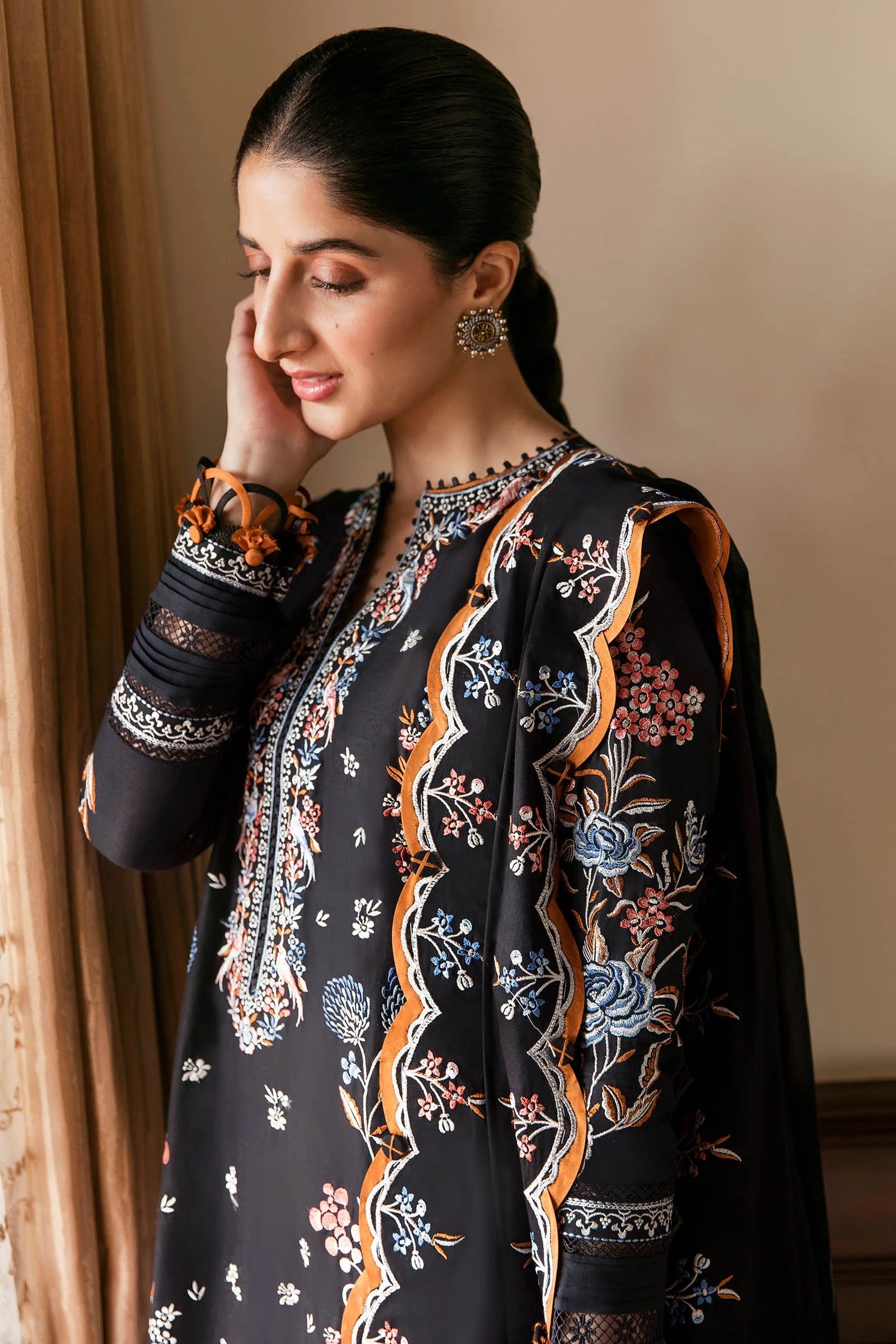 Woman wearing a black embroidered traditional outfit with floral patterns, standing against a neutral background.