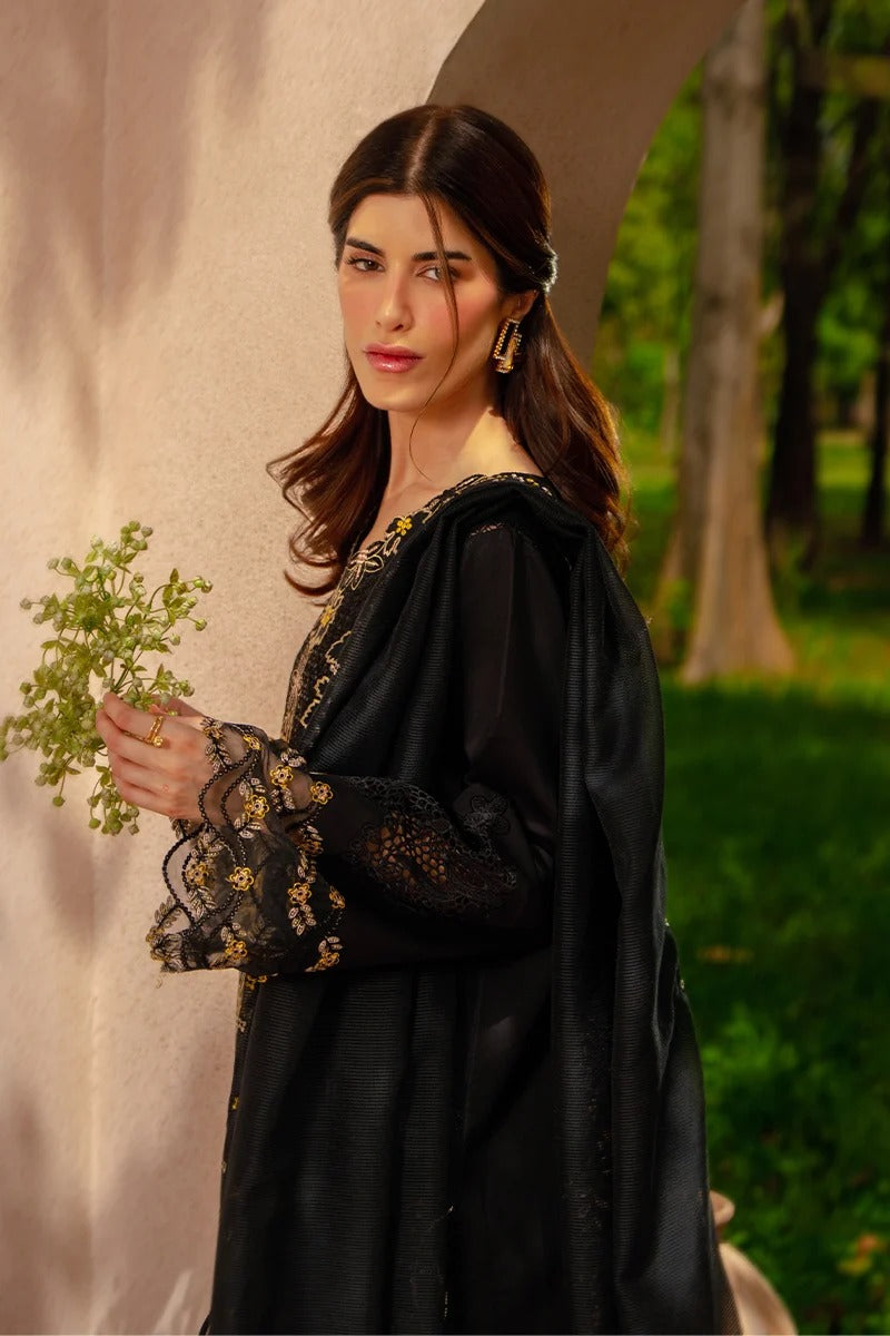 Woman in a black traditional outfit holding green leaves against a natural background