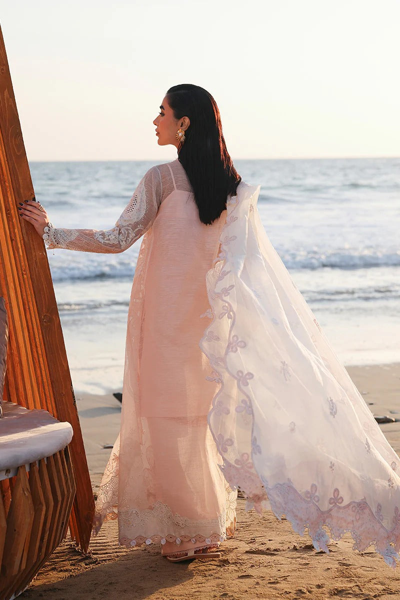 Woman in a light pink traditional outfit standing on a beach with ocean view