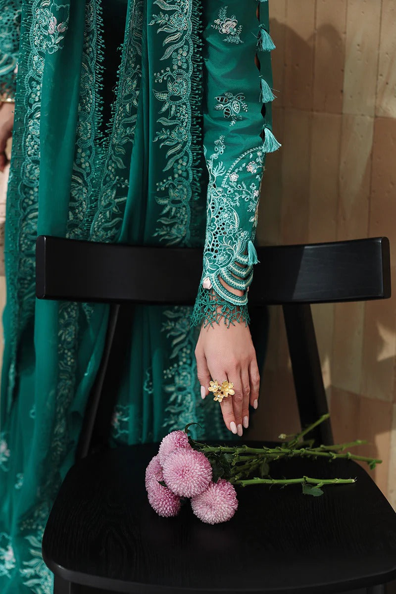 Person wearing a green embroidered outfit with a black chair and pink flowers in the foreground.