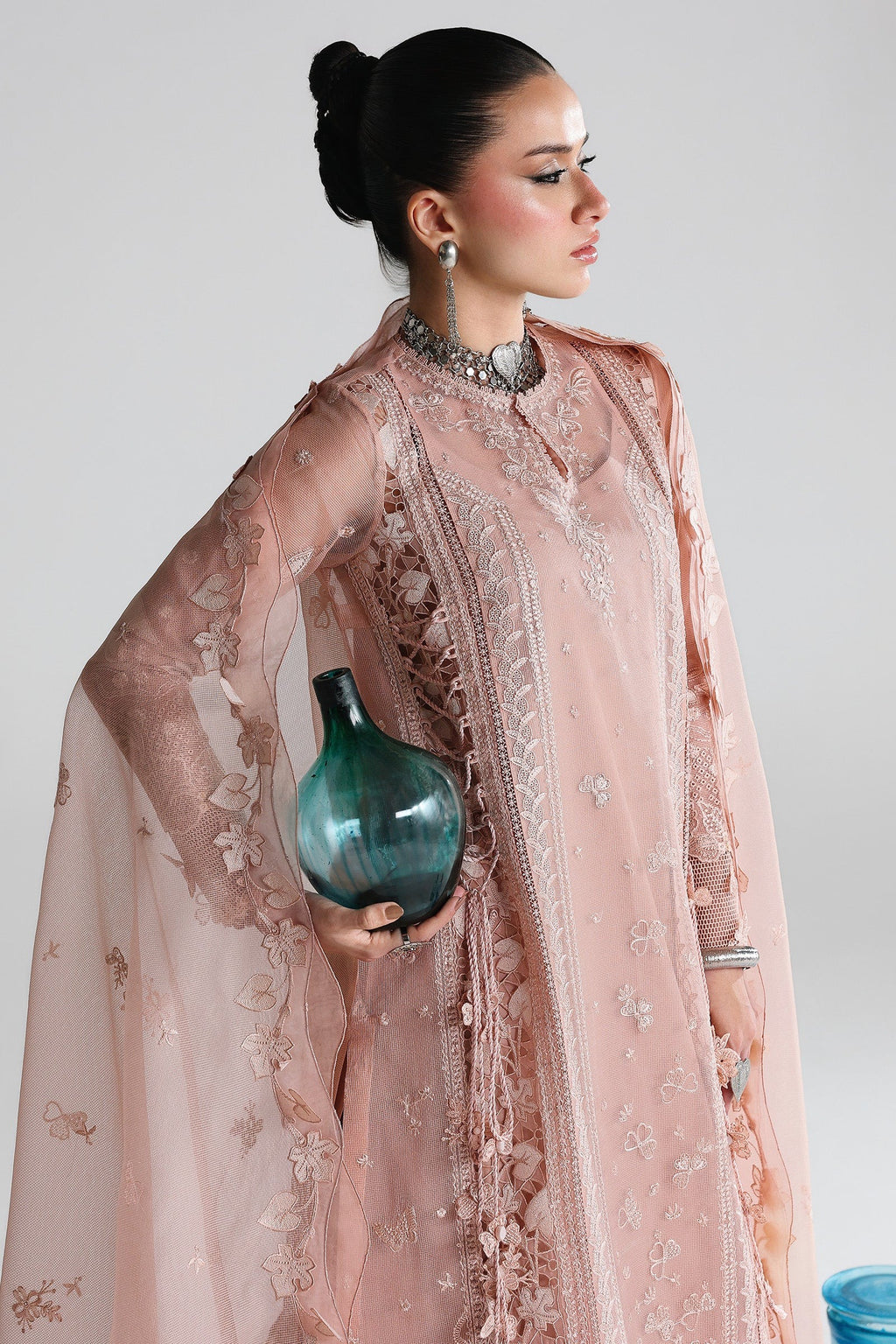 Woman in a pink embroidered outfit holding a blue vase against a white background