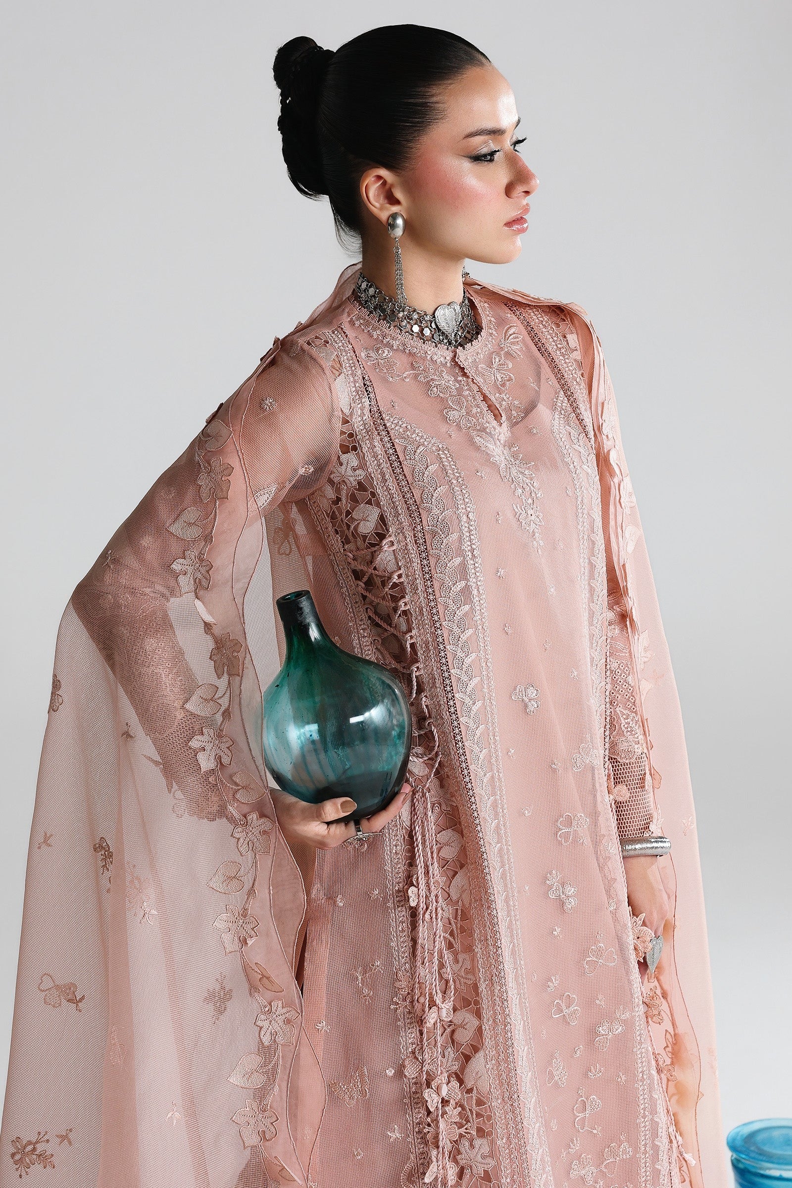 Woman in a pink embroidered outfit holding a blue vase against a white background