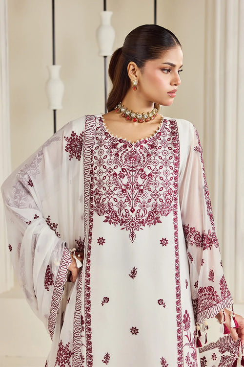 A woman modeling a traditional white ethnic kurta set with deep maroon embroidery and a matching sheer embroidered dupatta, set against a soft beige background with hanging decorative vases.