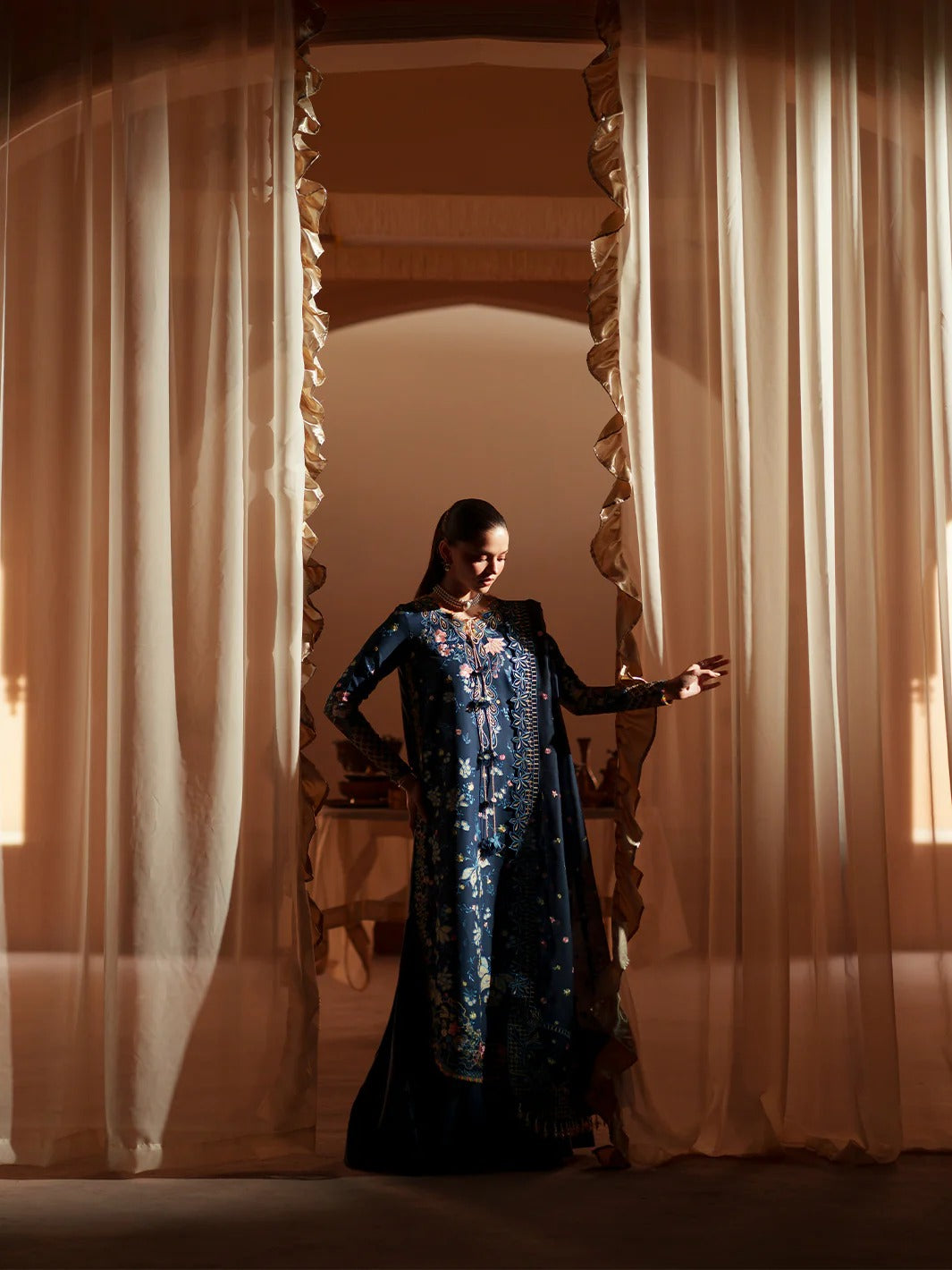 Woman in a blue dress standing between two curtains in a dimly lit room