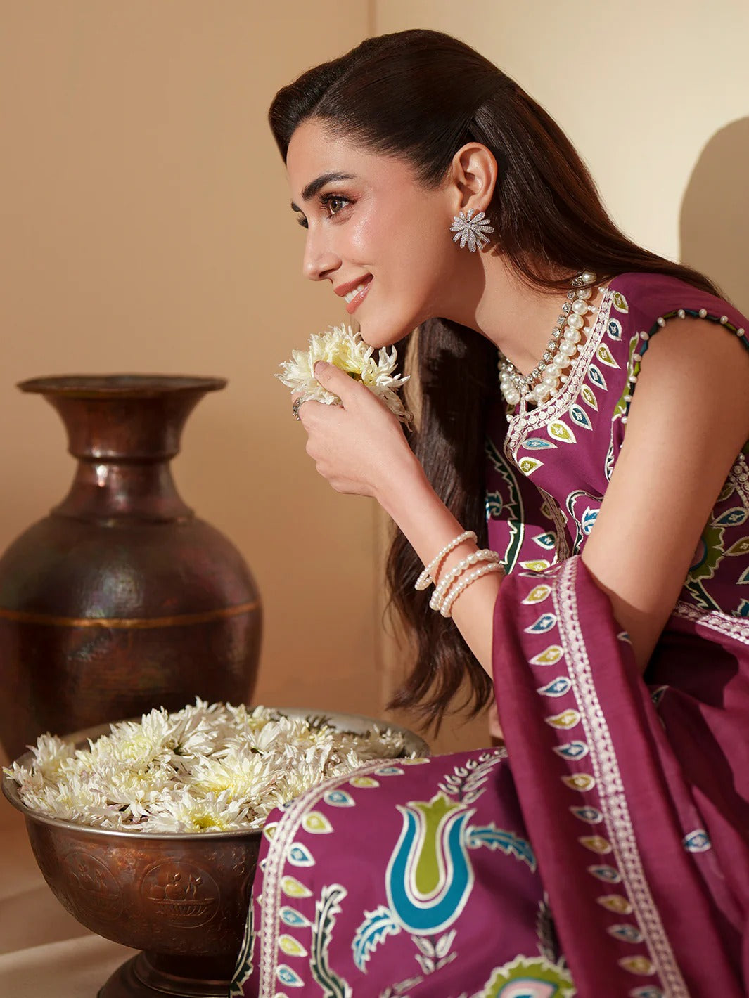 Woman in traditional attire holding a flower, with a decorative vase and flowers in the background.