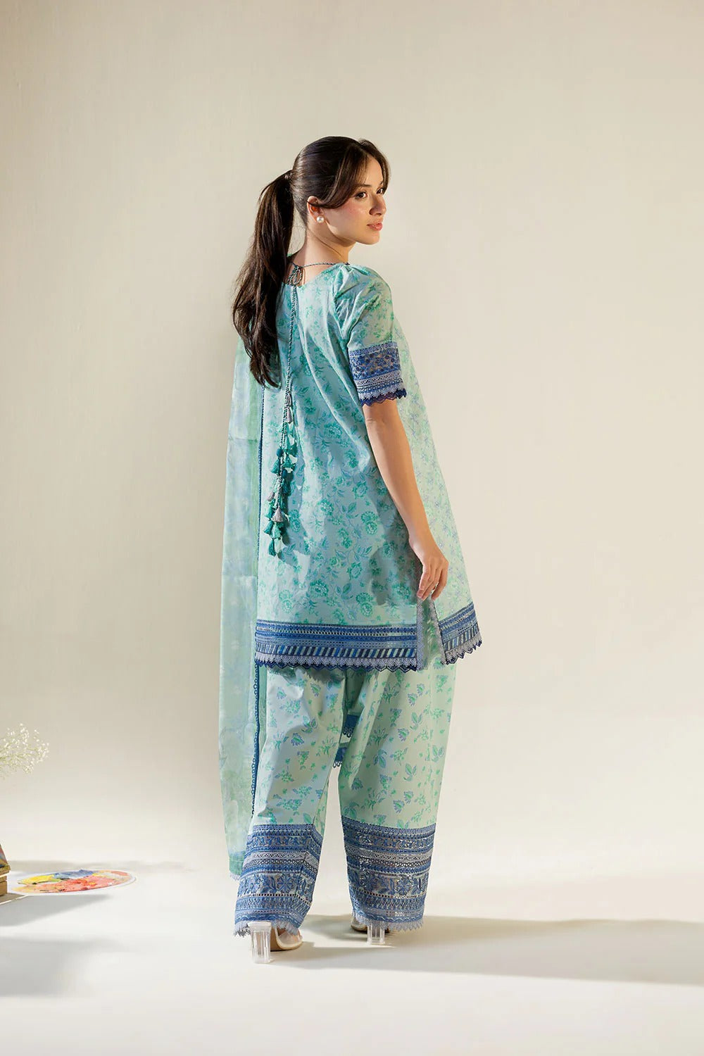 Woman wearing a light blue traditional outfit with patterns on a plain background