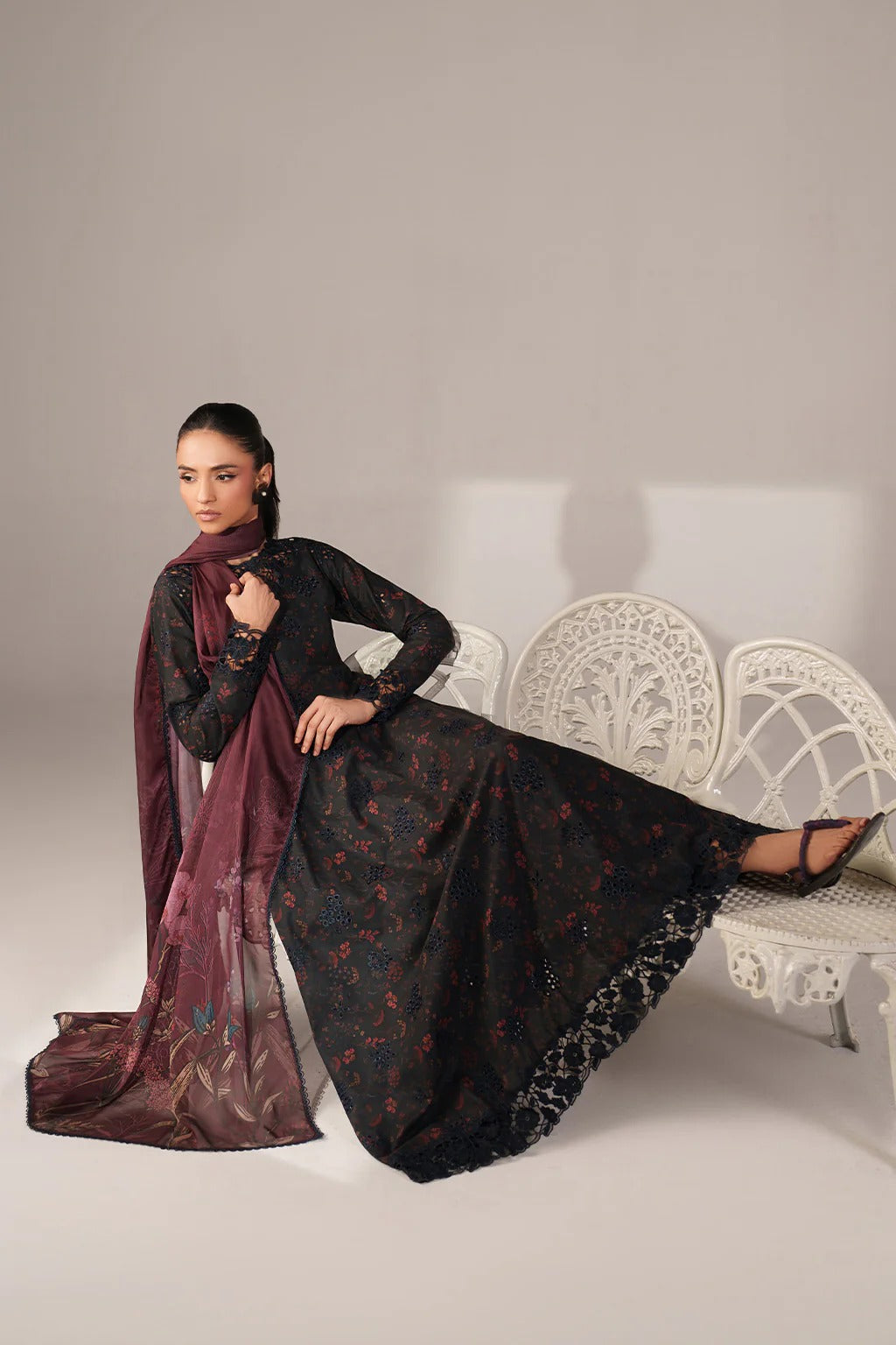 Woman in a black and red traditional outfit with a matching scarf, sitting on a white chair.