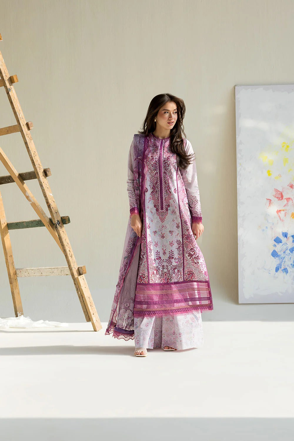 Woman in a patterned outfit standing in a minimalistic room with a ladder and abstract painting.
