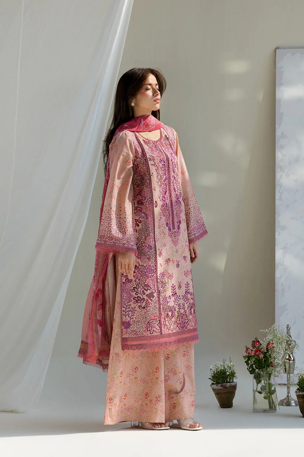 Woman wearing a pink and purple embroidered traditional outfit in a minimalistic setting.