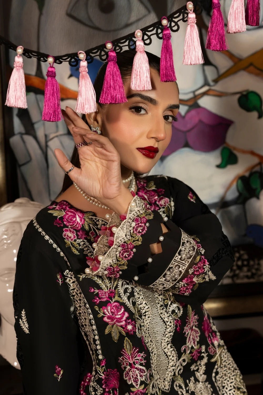 Woman wearing a black embroidered outfit with pink and white tassels in the background