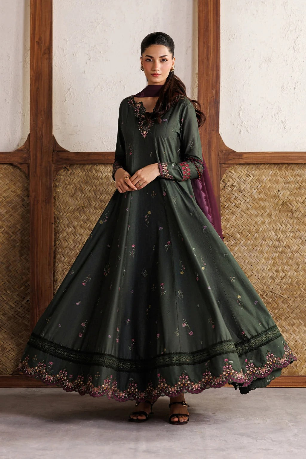 Woman wearing a dark green traditional outfit with floral embroidery in a room with wooden paneling.