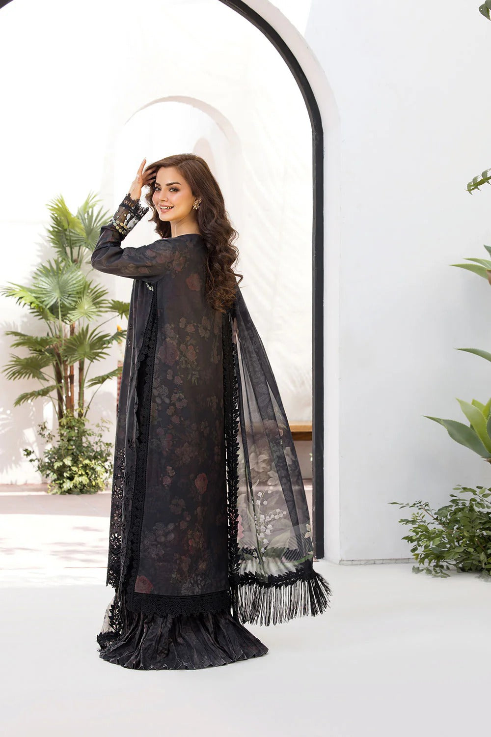 Woman in a black lace dress standing in a decorative indoor setting with plants.