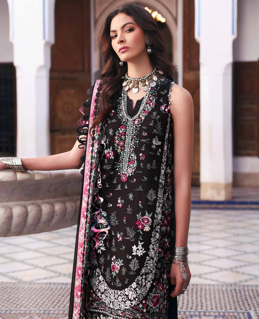 Woman wearing a black embroidered dress with floral patterns in an outdoor setting.