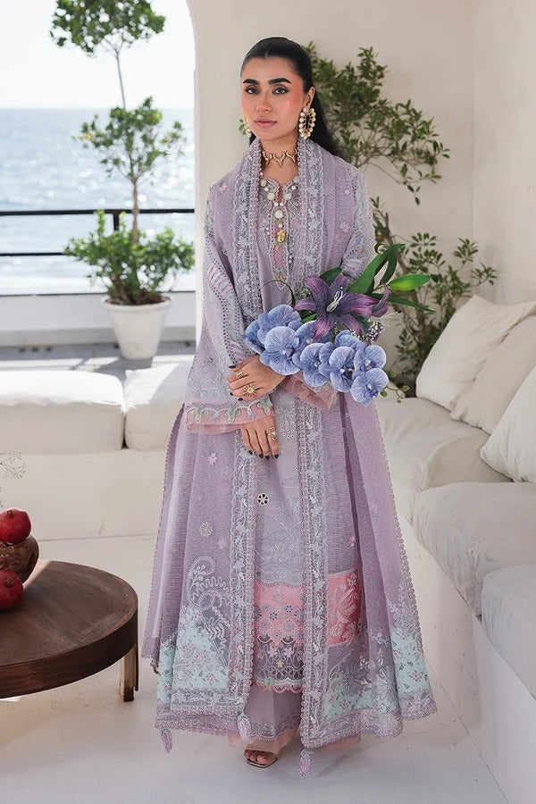 Woman in a light purple embroidered outfit holding flowers in an outdoor setting with plants and a couch.