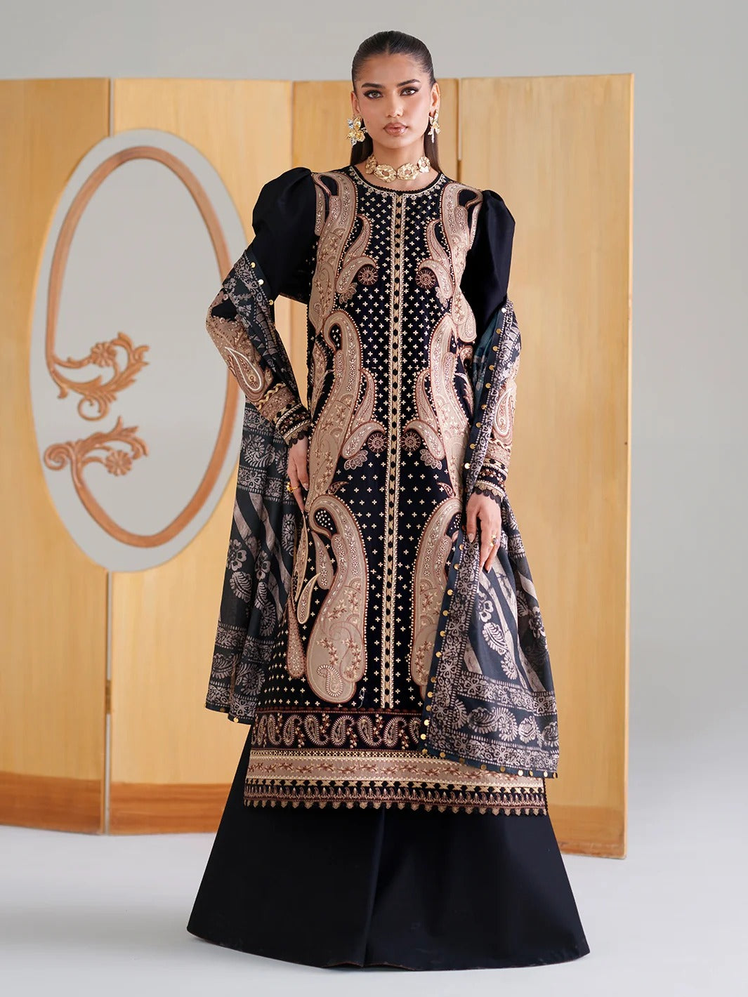 Woman wearing a black and gold embroidered traditional outfit with a wooden panel background