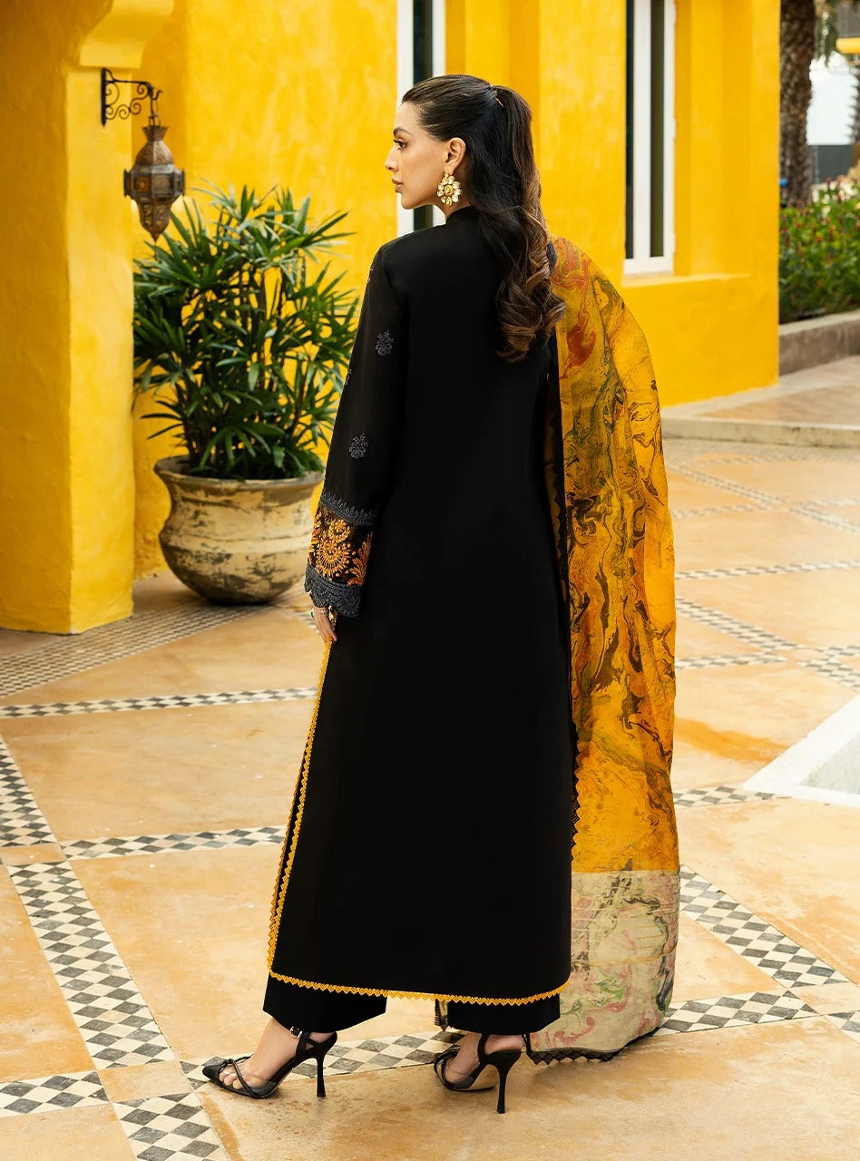 Woman in a black outfit with gold embroidery holding a yellow and orange scarf in a decorative setting.