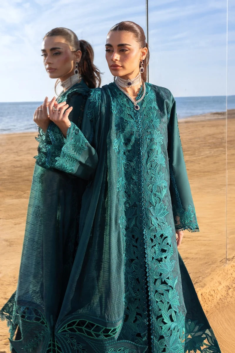 Two women in teal embroidered dresses standing on a beach with ocean in the background