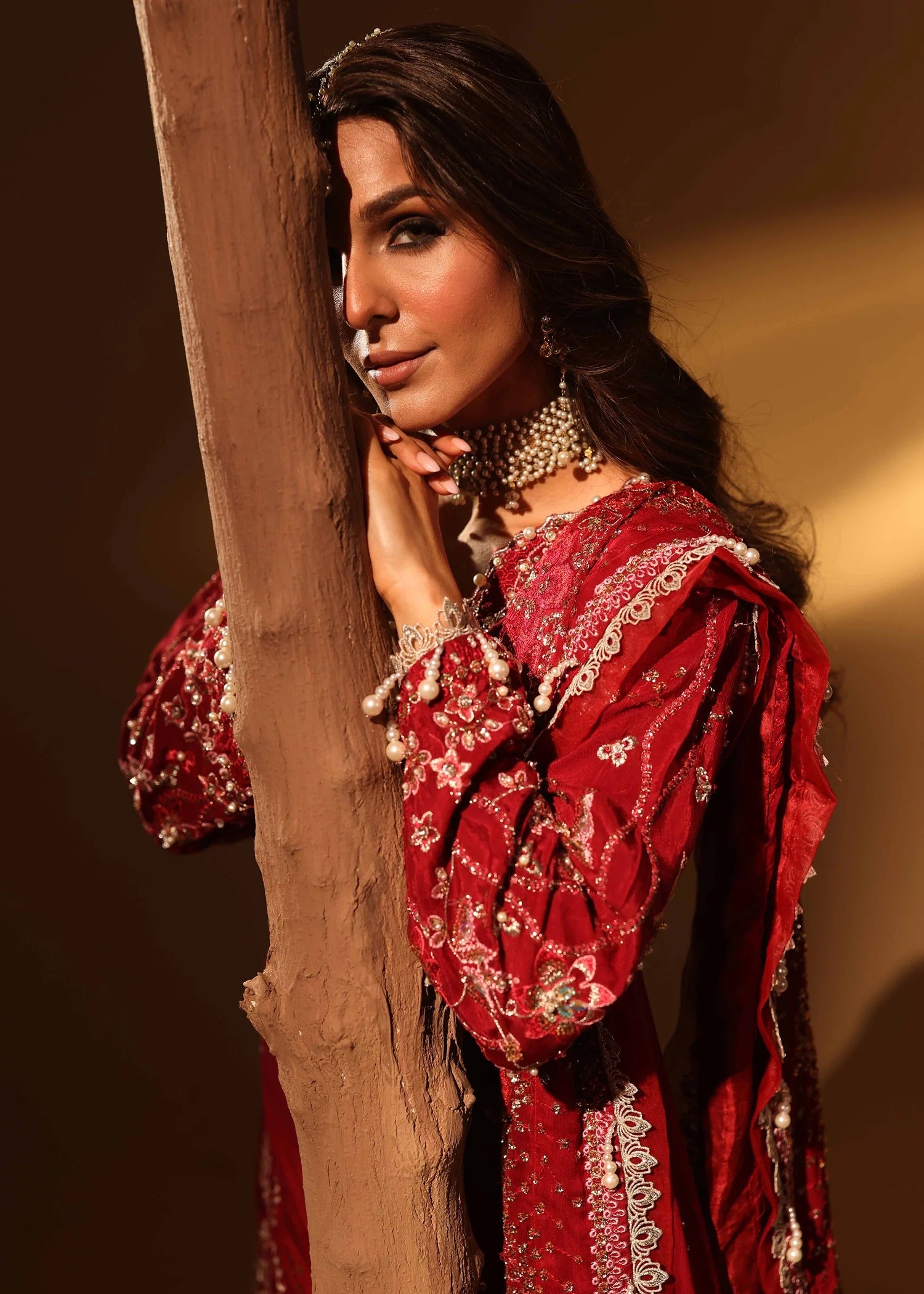 Woman in a red embroidered traditional outfit posing against a wooden post.