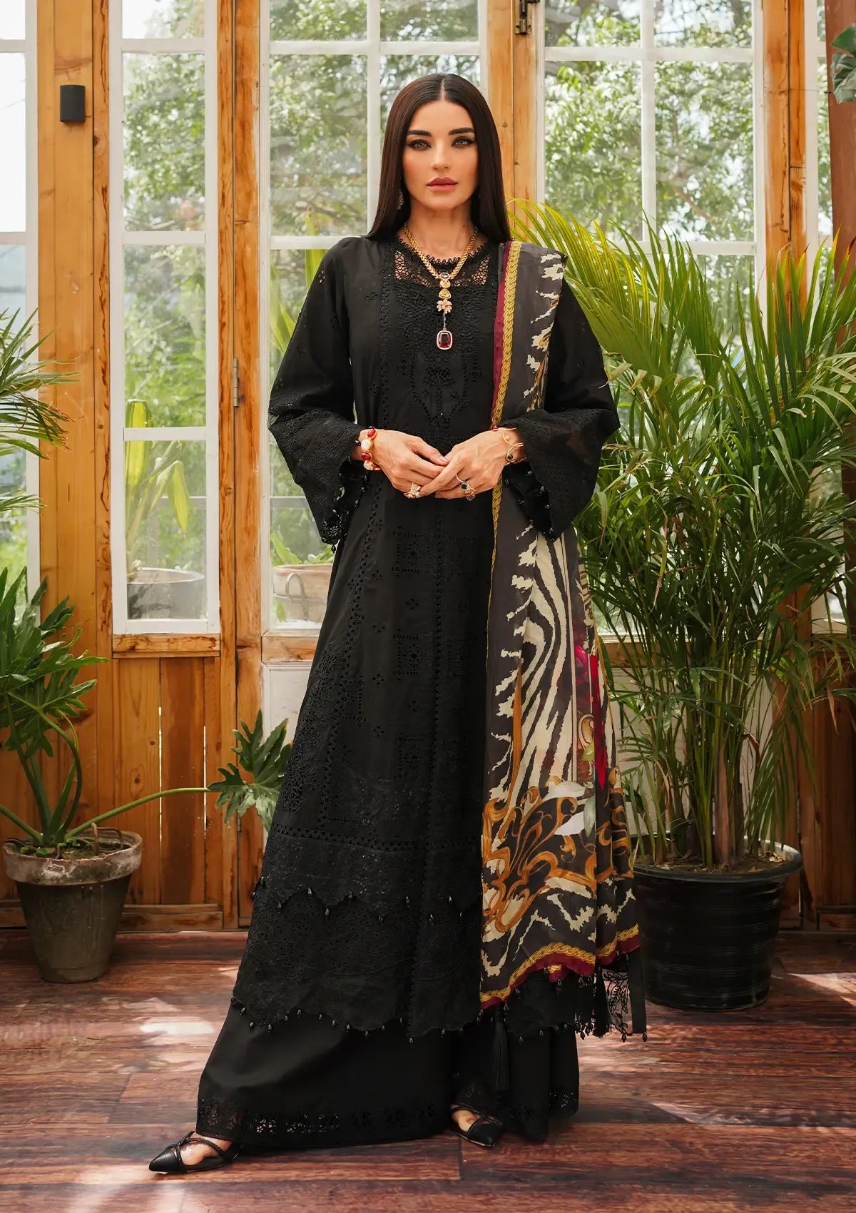 A woman modeling a black embroidered kurta set with a patterned dupatta in a rustic indoor setting with wooden doors and potted plants.