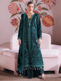 A woman models a traditional dark teal green embroidered kurta set with a matching dupatta, standing in front of a pink sofa and a floral wall mural.