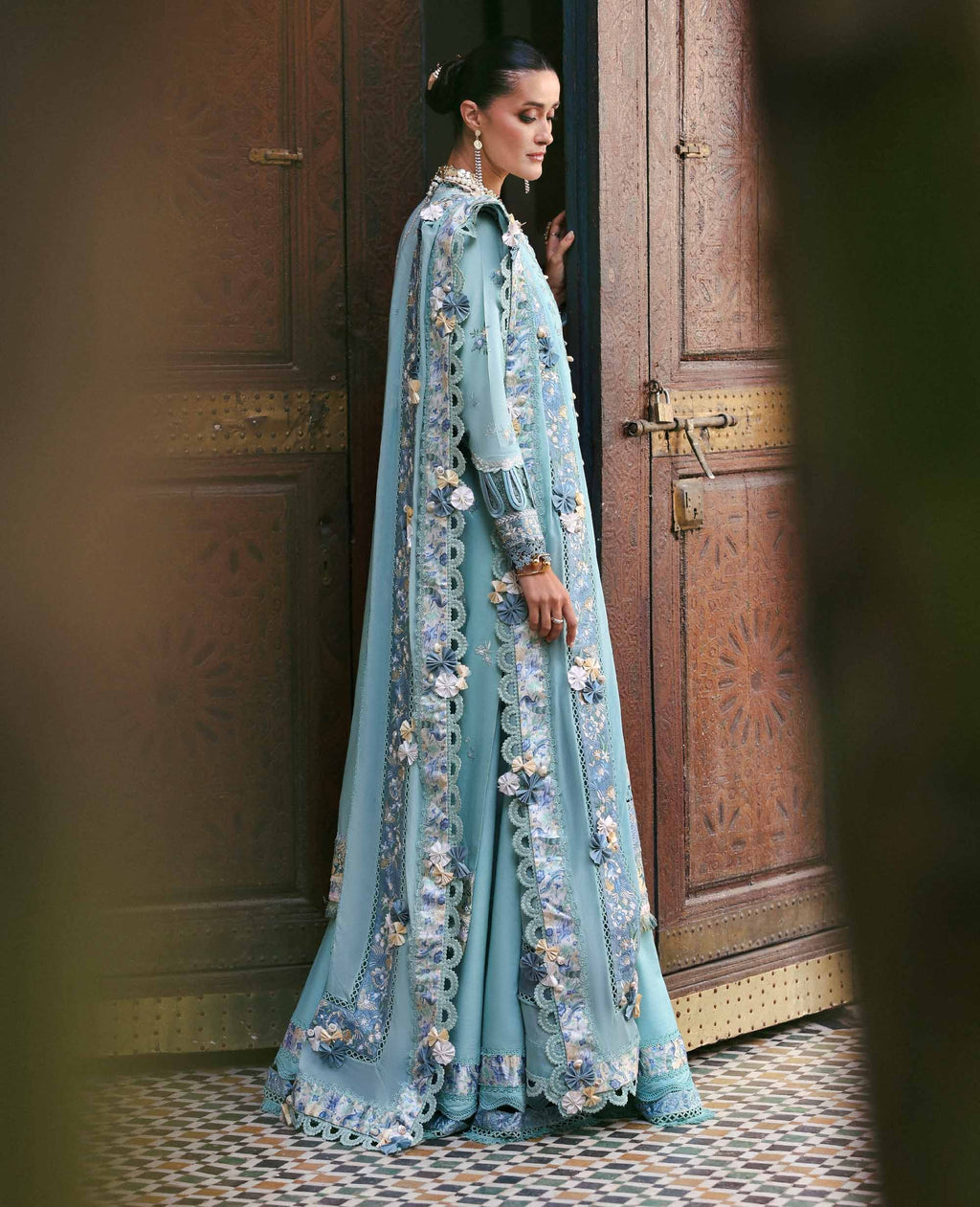 Woman in a light blue embroidered dress standing in a doorway.