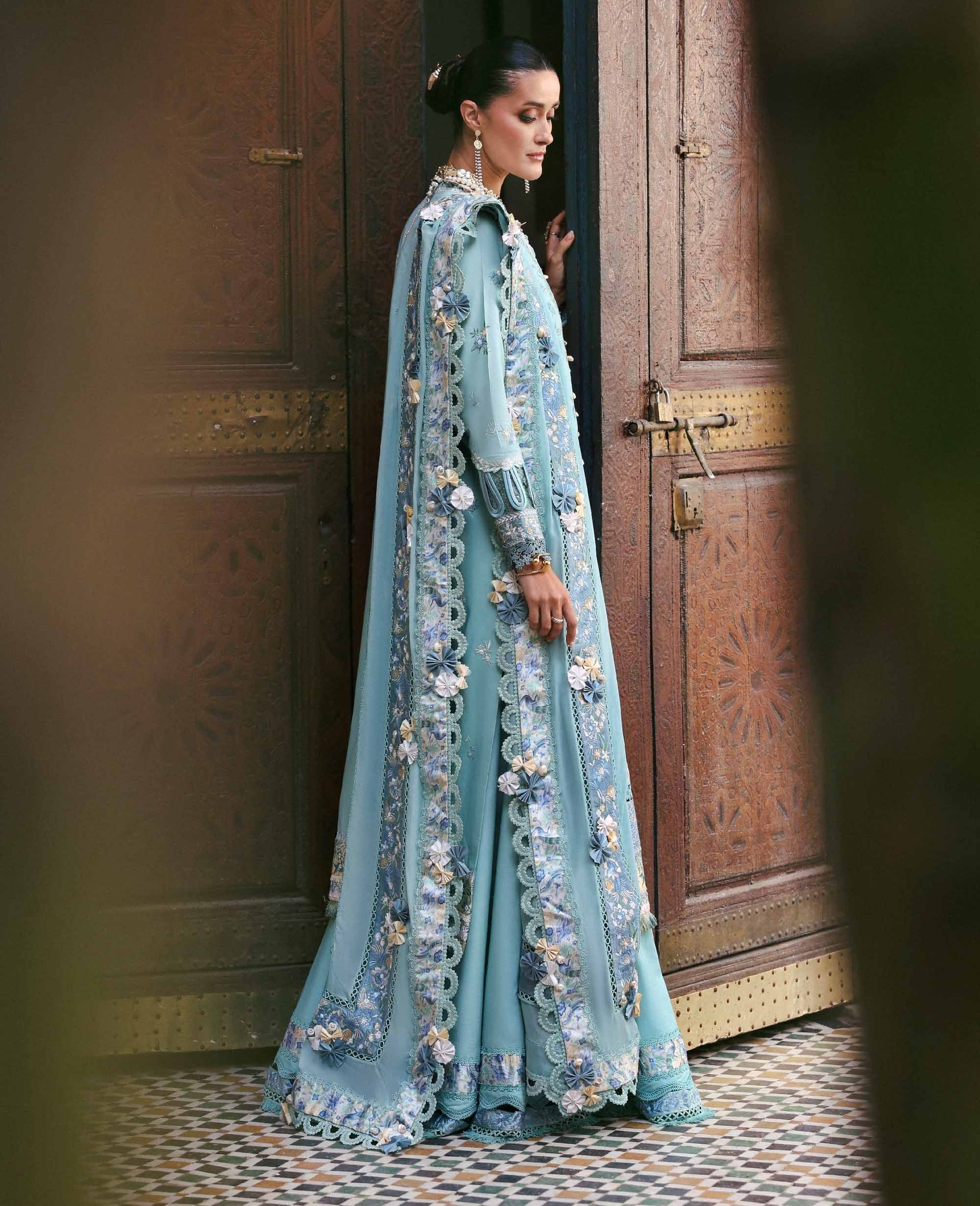Woman in a light blue embroidered dress standing in a doorway.