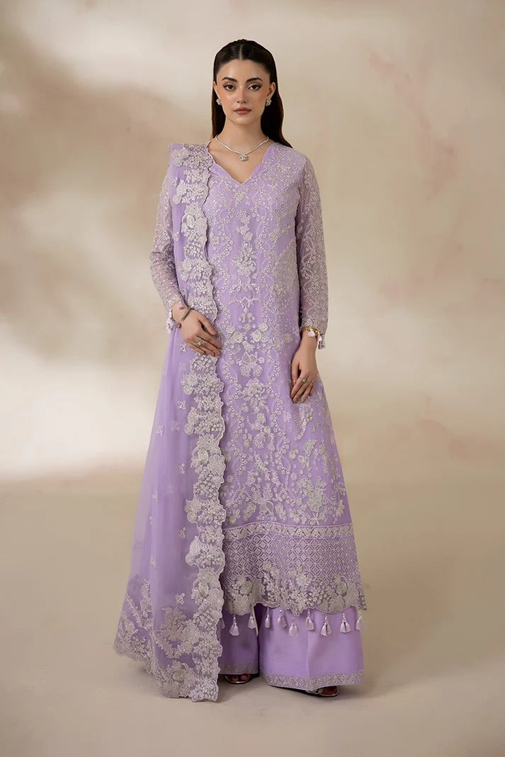 A woman modeling a lavender purple traditional Anarkali suit with intricate silver floral embroidery, paired with matching wide-leg trousers, set against a warm beige studio backdrop.