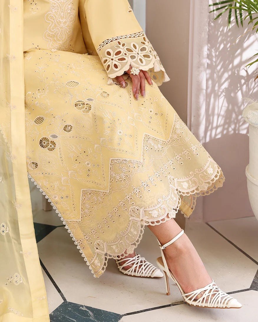 A person wearing a pale yellow embroidered dress or kurta with intricate eyelet lace detailing and a scalloped hem, paired with white strappy high-heeled sandals in a softly lit indoor setting.