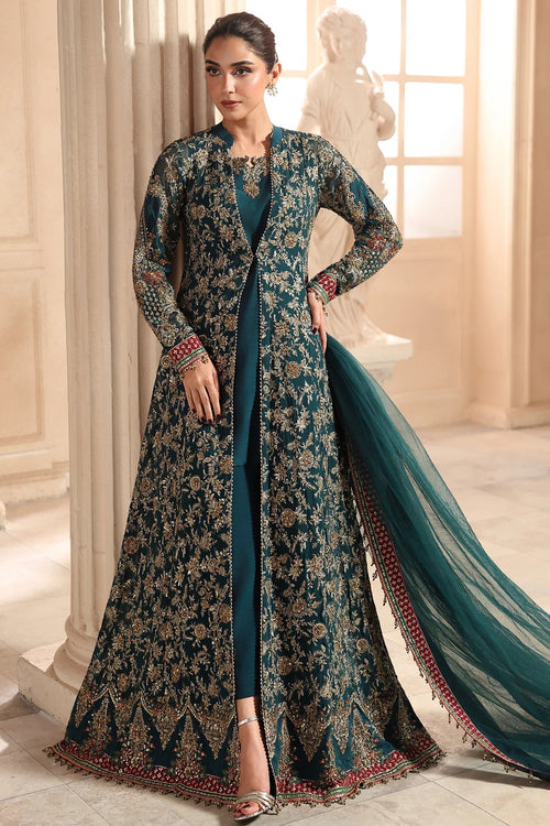 A woman models a long teal and gold embroidered Anarkali gown with a matching dupatta in an elegant indoor setting with classical columns and a statue.