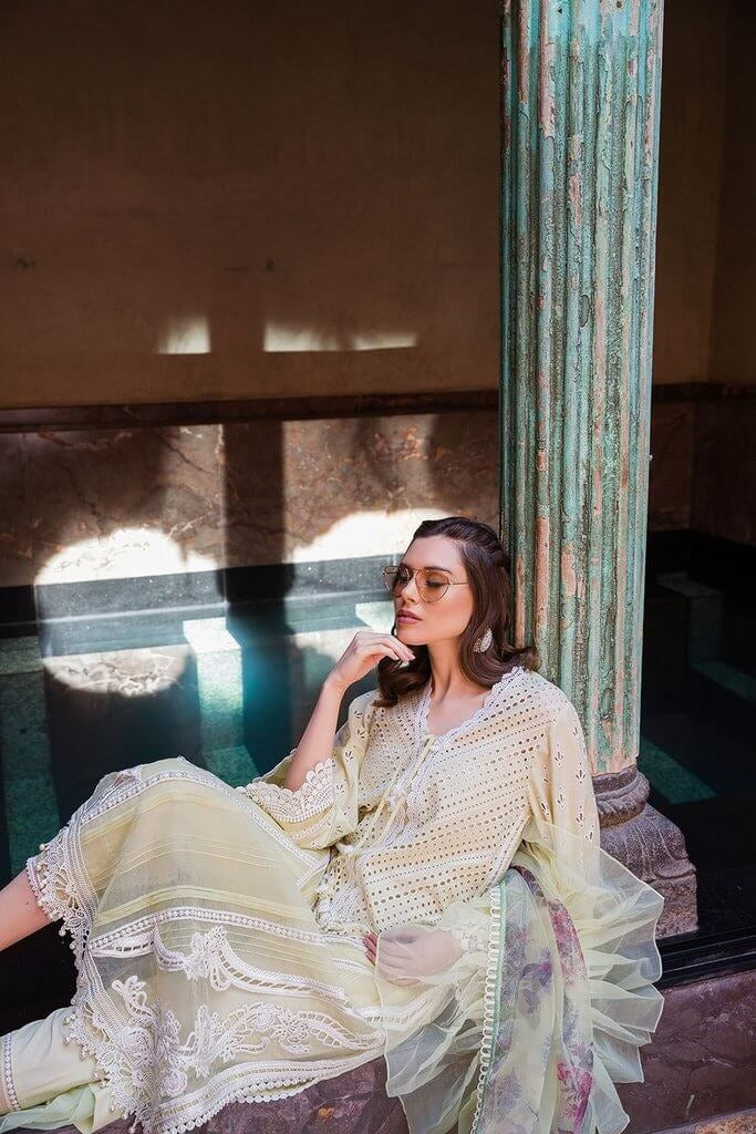 Woman in a light-colored outfit sitting on steps with a textured wall and column in the background