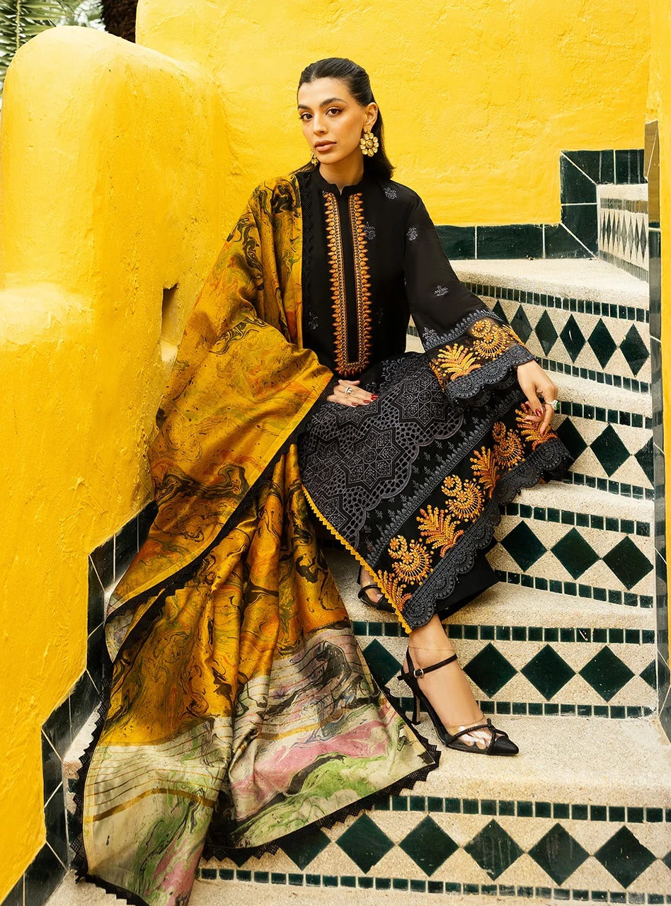 A woman models a traditional South Asian outfit consisting of a black embroidered kurta, a matching black skirt with gold embroidery, and a large mustard yellow printed dupatta, posed on patterned stairs against a bright yellow wall.