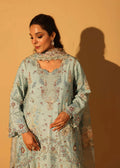 Woman wearing a light blue embroidered traditional outfit against a beige background