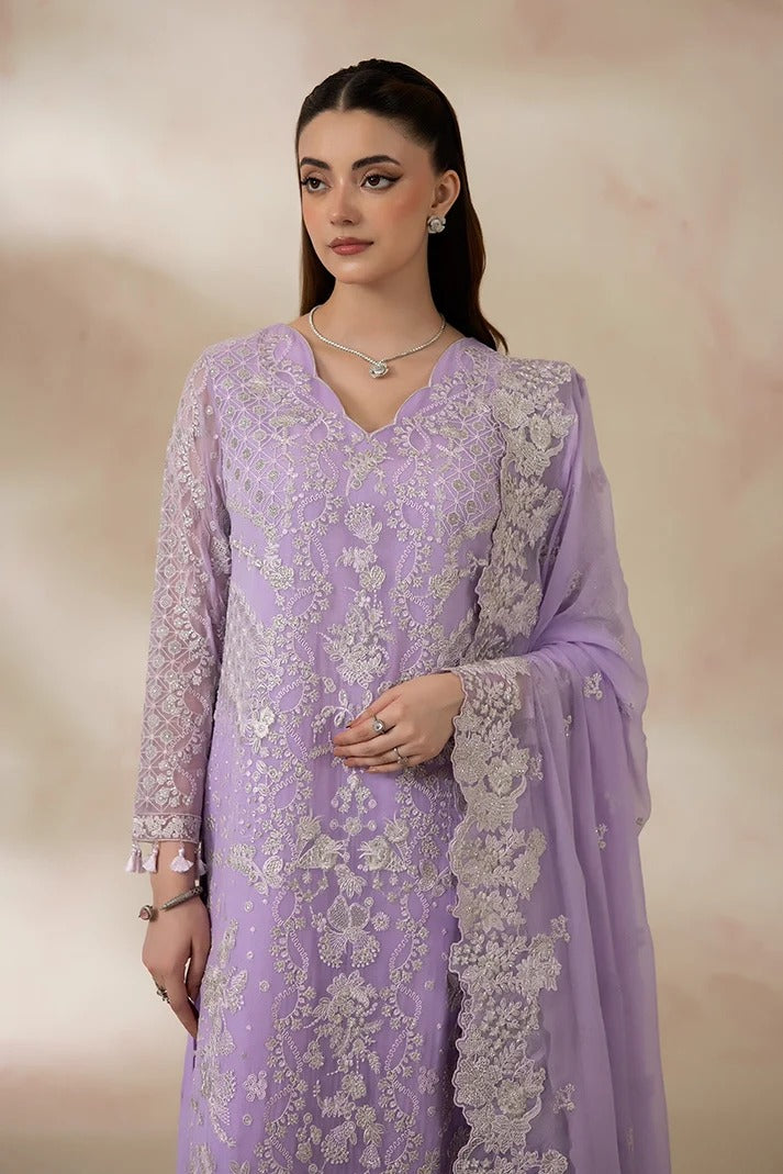 A woman modeling a lavender purple traditional embroidered outfit with white floral lace embroidery, a matching sheer dupatta, and a silver necklace against a soft beige studio background.