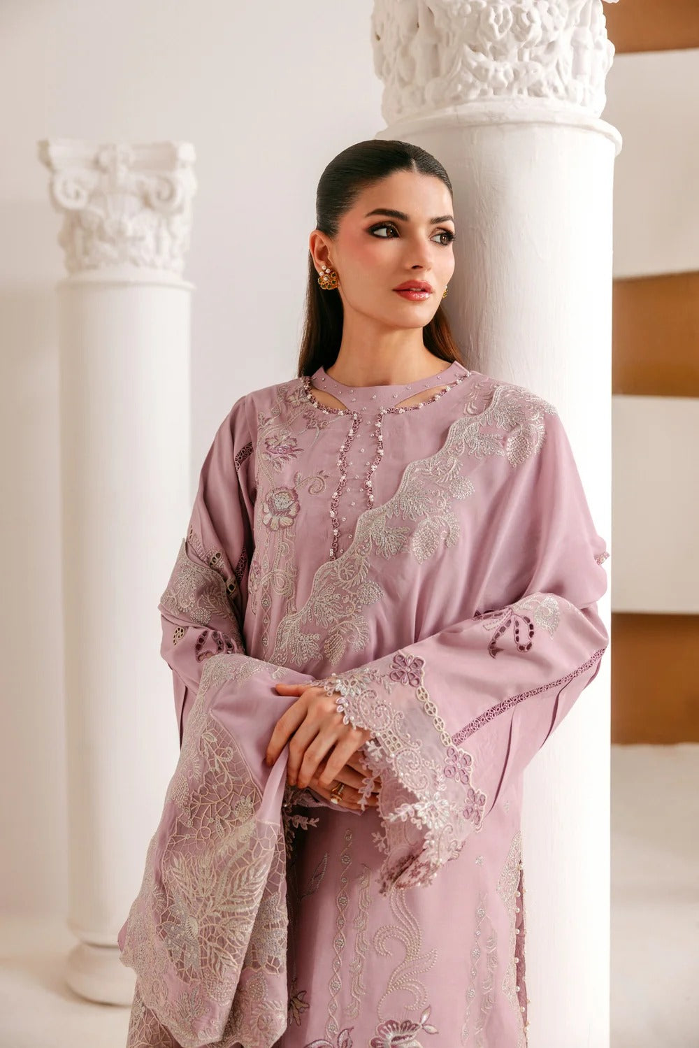 A woman models a dusty pink embroidered traditional outfit with matching dupatta, standing between white classical columns.
