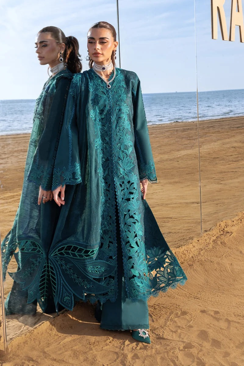Woman in a teal embroidered outfit standing on a beach with ocean view.