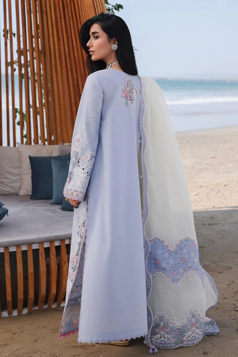 Woman in a light blue embroidered dress standing on a beach.