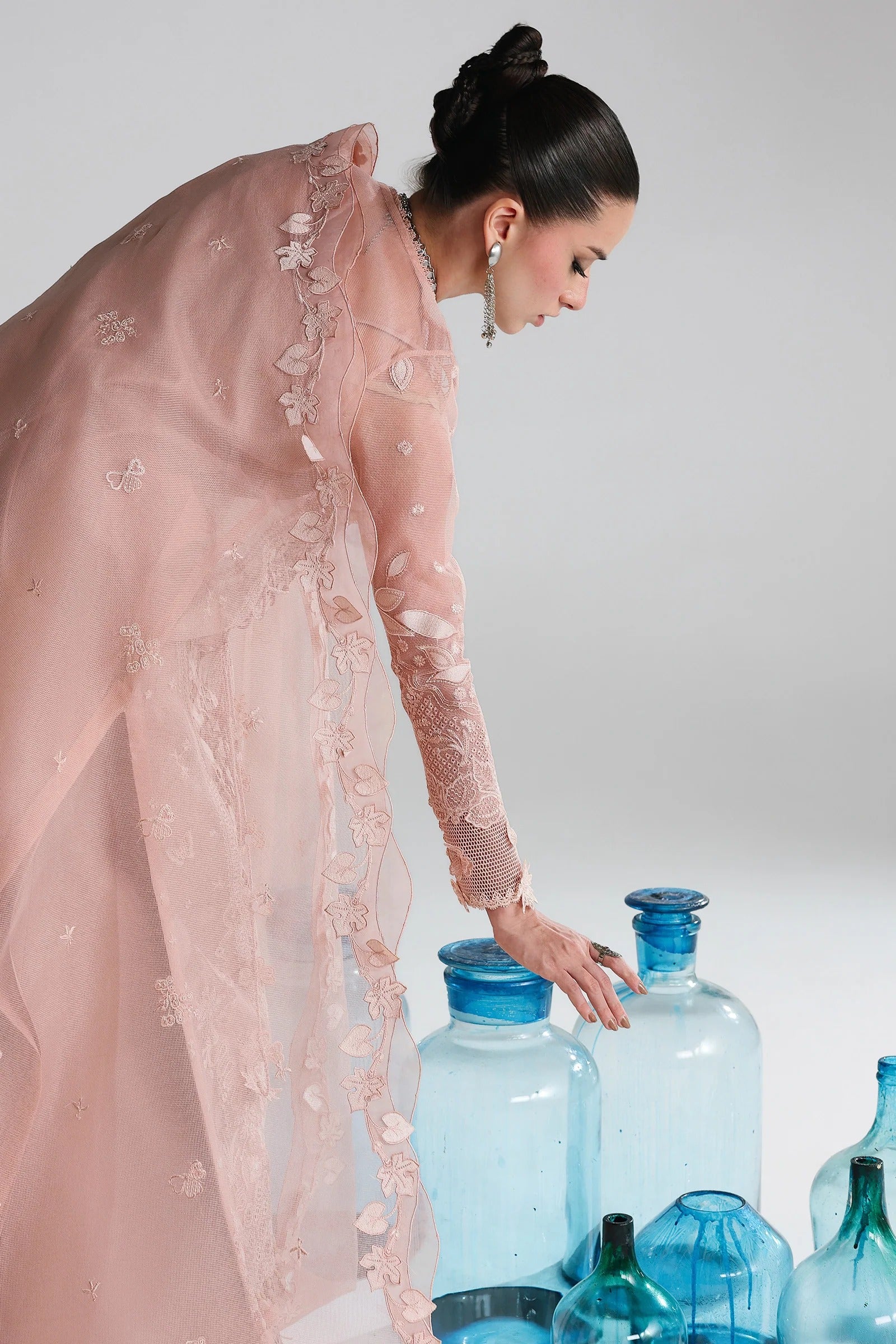 Woman in a pink dress interacting with blue bottles against a white background