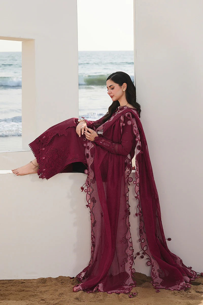 Woman in a burgundy embroidered dress sitting by a window with a view of the ocean.