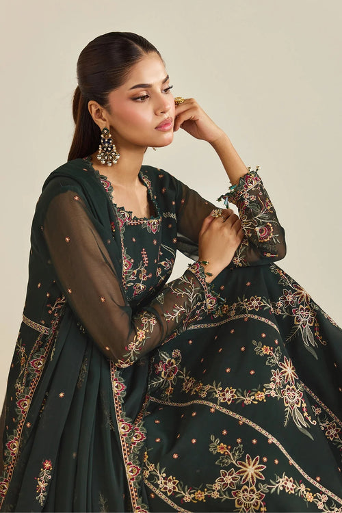 A woman models a dark green embroidered traditional outfit with sheer sleeves and a matching dupatta, set against a plain beige background.