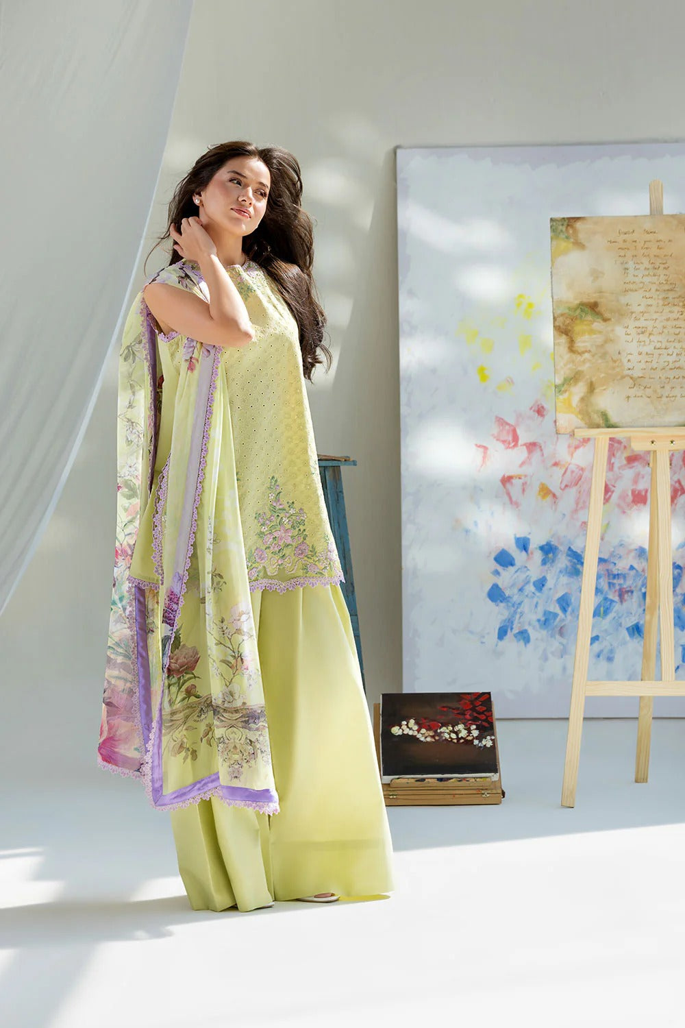 Woman in a light green traditional outfit standing in a bright room with a colorful abstract painting on an easel.