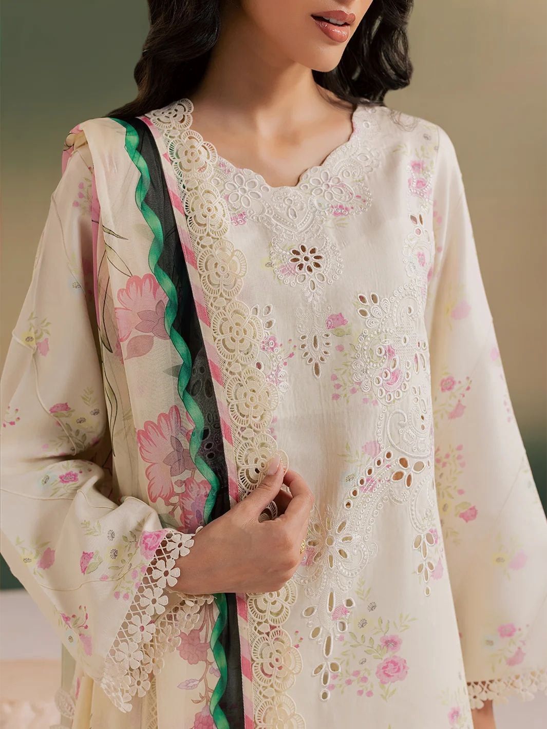A close-up of a woman wearing a cream-colored embroidered kurta with pink floral prints and a matching dupatta featuring a green and black border.