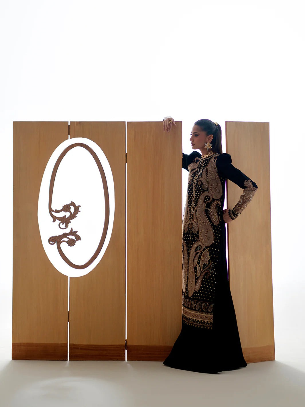 Woman in a long black dress standing next to a wooden screen with a logo on it.