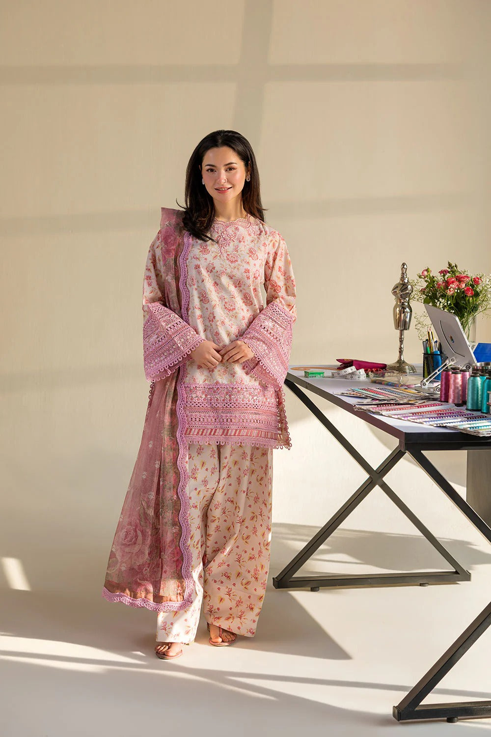 Woman in a pink traditional outfit standing next to a table with decorative items.
