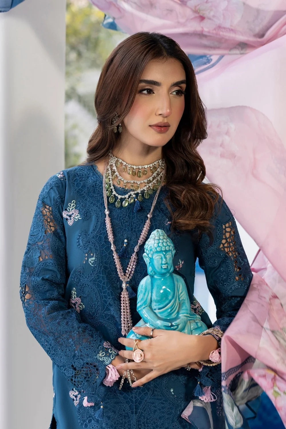 Woman holding a turquoise Buddha statue wearing a blue embroidered outfit with jewelry.